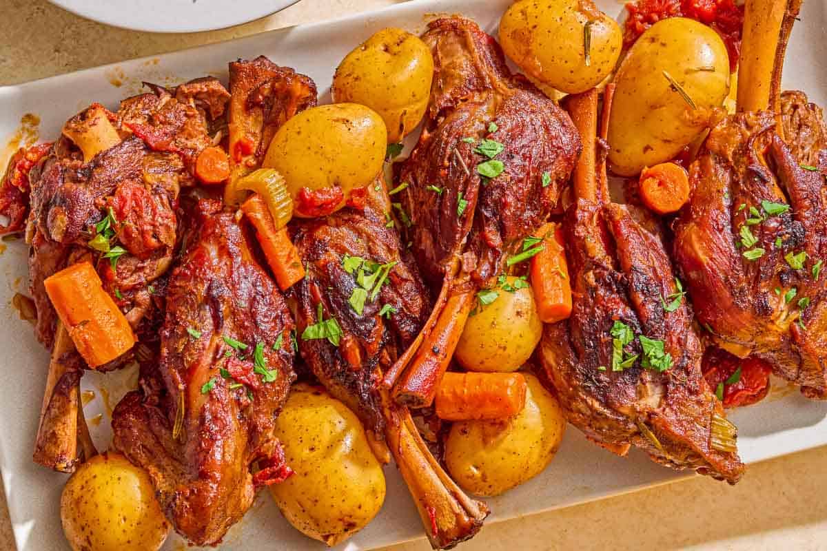 Braised lamb shanks with carrots and potatoes on a platter.
