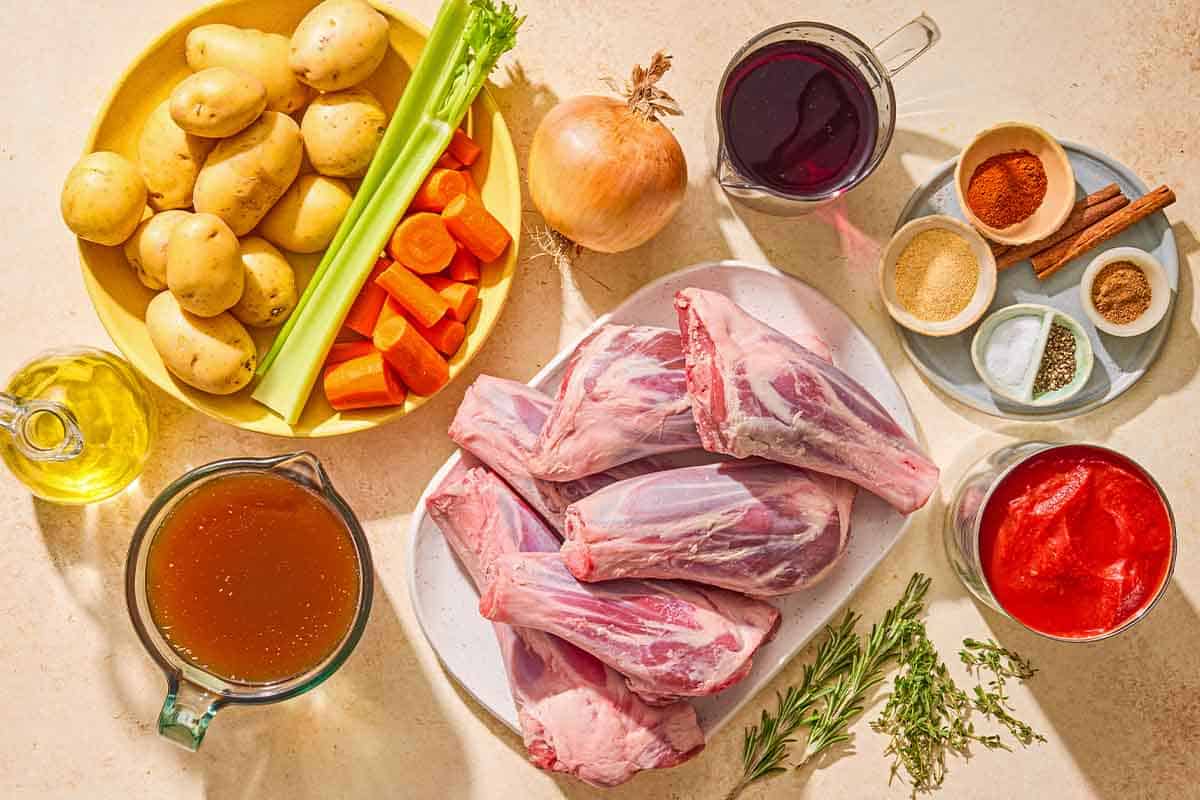 Ingredients for the lamb shank recipe including lamb shanks, olive oil, garlic powder, paprika, salt, pepper, nutmeg, olive oil, yellow onion, celery, carrots, potatoes, red wine, both, canned peeled tomatoes, cinnamon sticks, thyme, and rosemary.