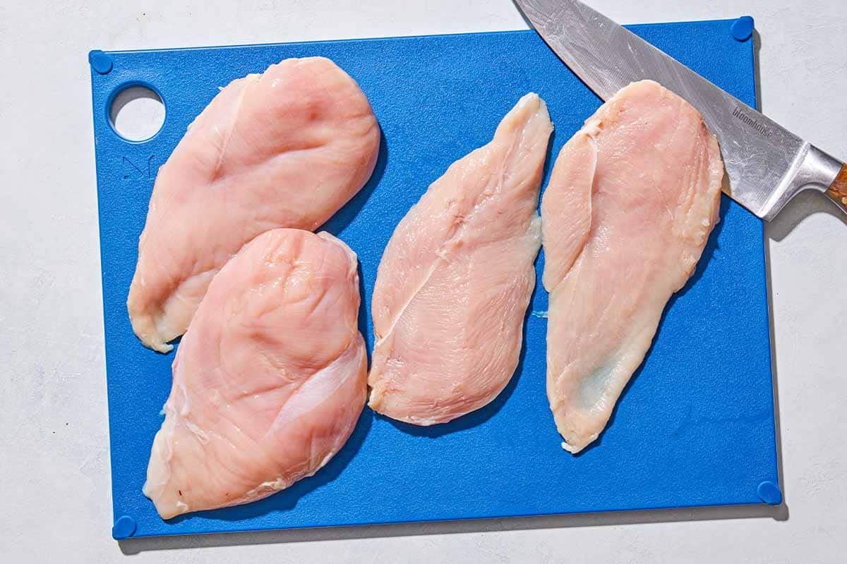 2 whole chicken breasts and 2 chicken cutlets on a cutting board with a knife.