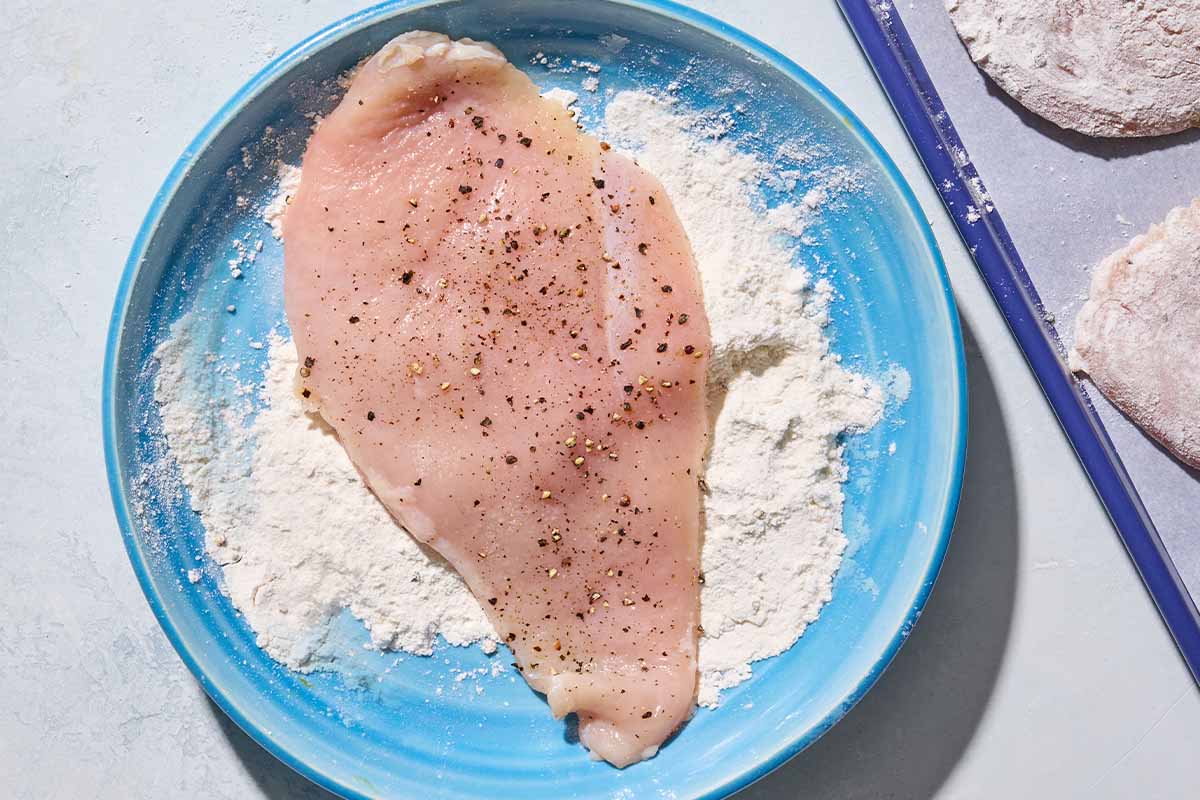 A seasoned chicken breast cutlet on a plate of flour.