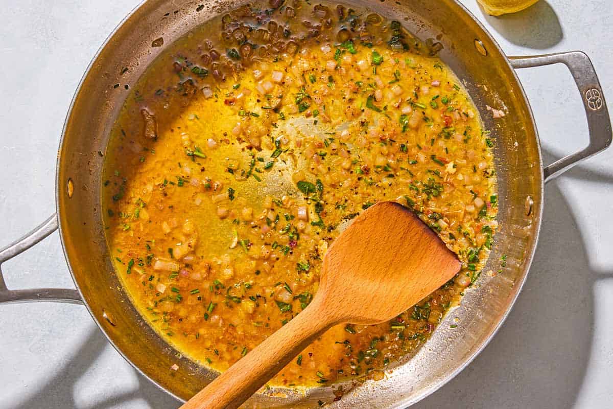 The pan sauce for the chicken scaloppine in a skillet being stirred with a wooden spoon.