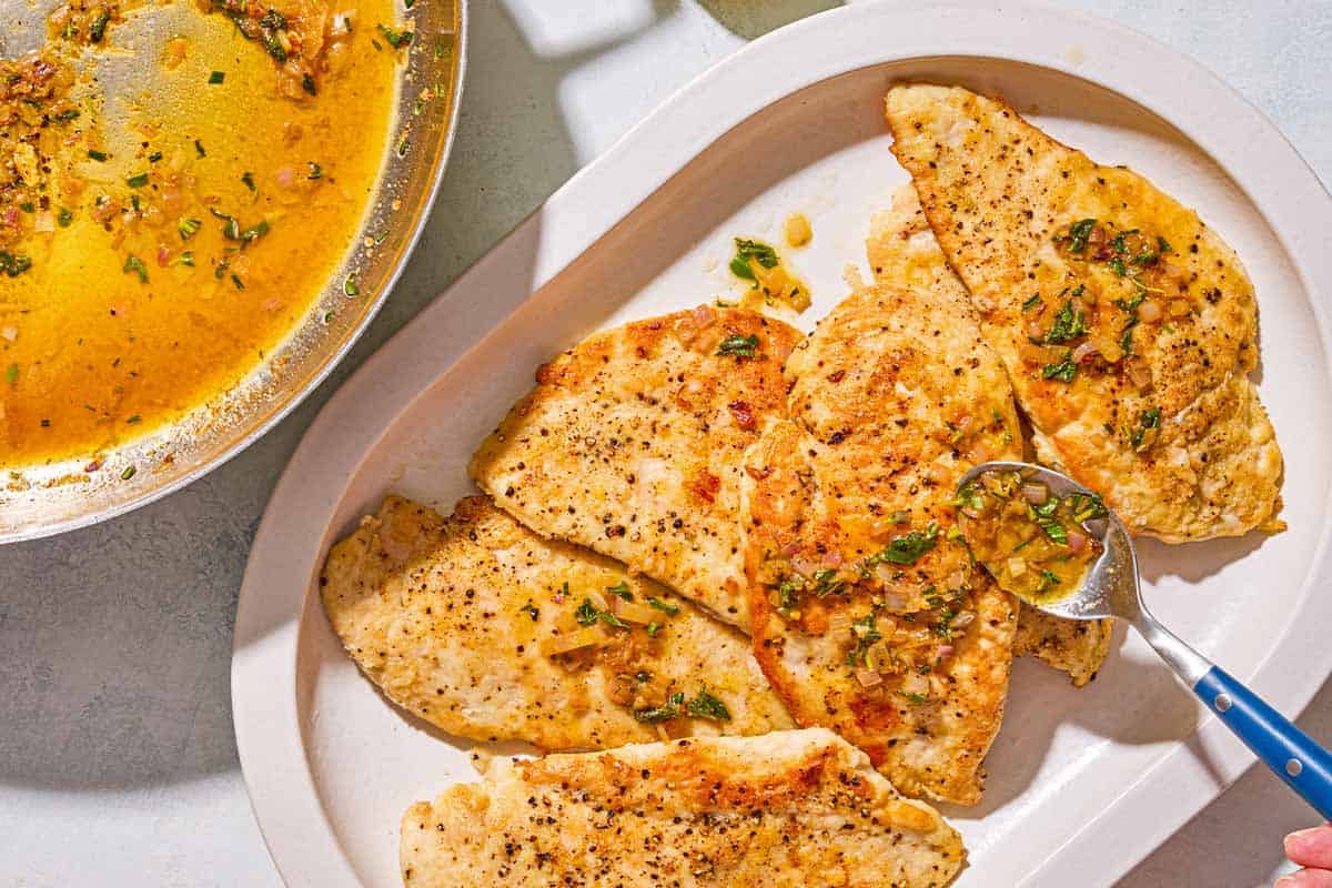 The pan sauce being spooned on the pieces of chicken scaloppine in a platter.