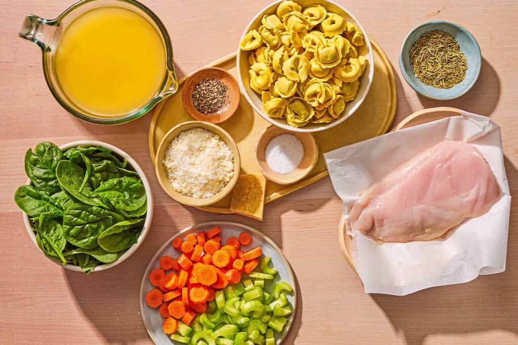 Ingredients for the chicken tortellini soup recipe including tortellini, Parmigiano-Reggiano cheese rind, chicken breast, carrots, celery, baby spinach, salt, pepper, and grated Parmigiano Reggiano.