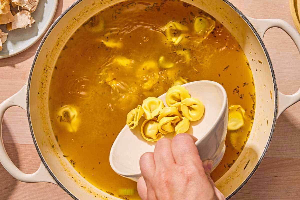 Tortellini being added to the tortellini soup from a bowl.