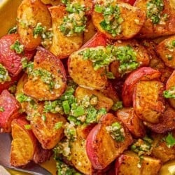 Crispy red skinned potatoes drizzled with walnut cilantro chili sauce in a bowl with a serving spoon.