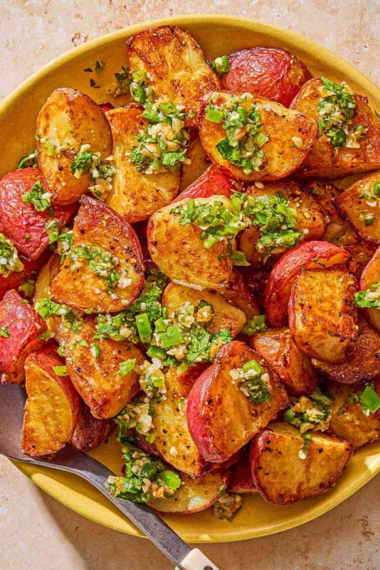 Crispy red skinned potatoes drizzled with walnut cilantro chili sauce in a bowl with a serving spoon.