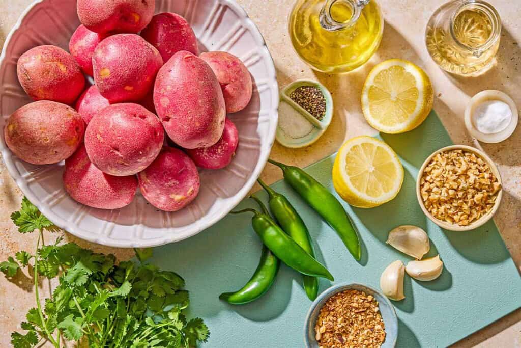 Ingredients for the crispy red skinned potatoes including red potatoes, salt, baking soda, black pepper, olive oil, serrano chilies, garlic, cilantro, lemon, white wine vinegar, chopped walnuts and olive oil.