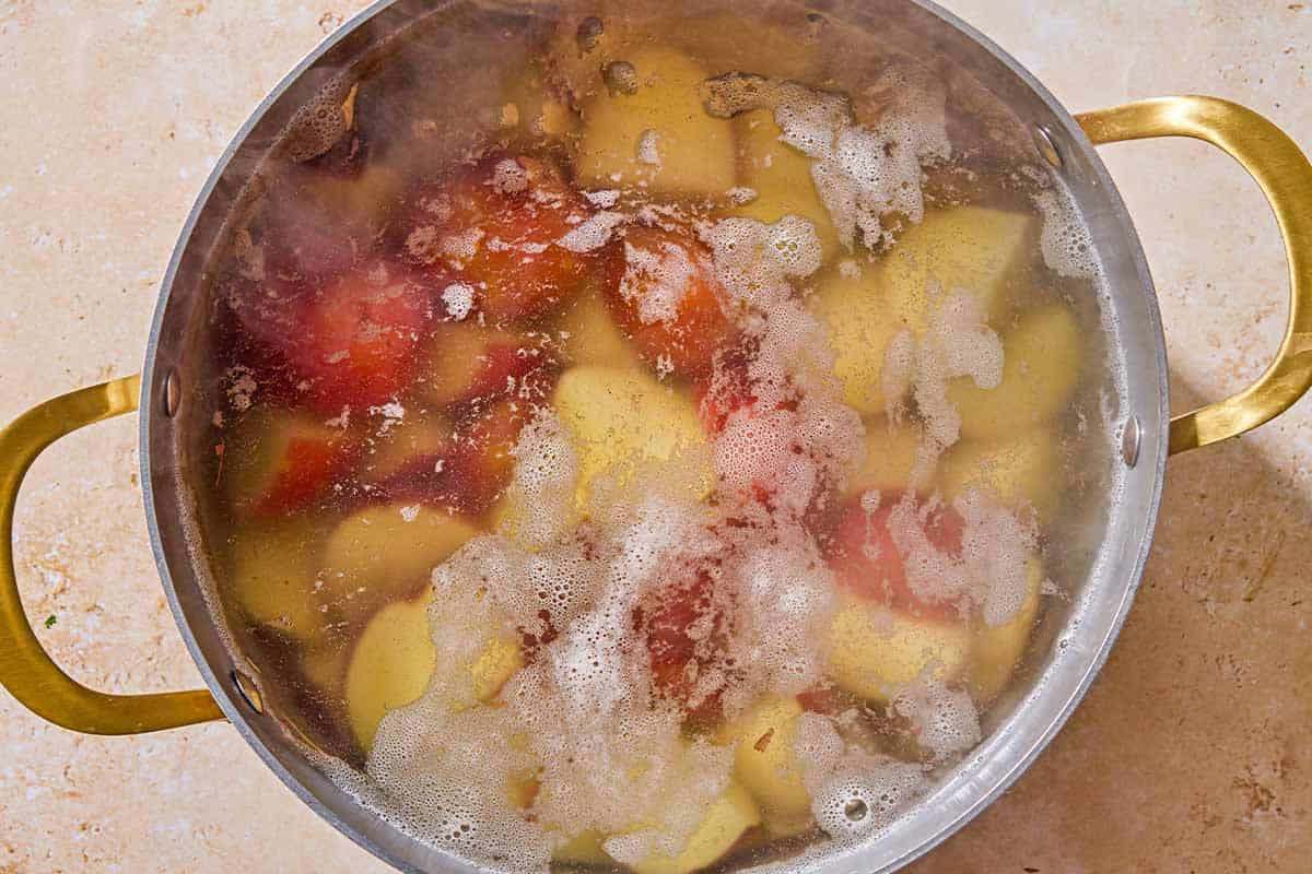 Quartered red skinned potatoes boiling in a pot of water.