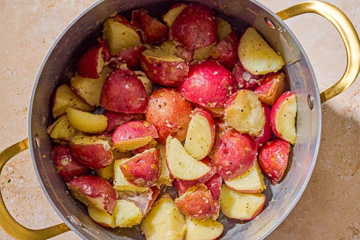 The boiled, quartered, and seasoned red skinned potatoes in a colander.