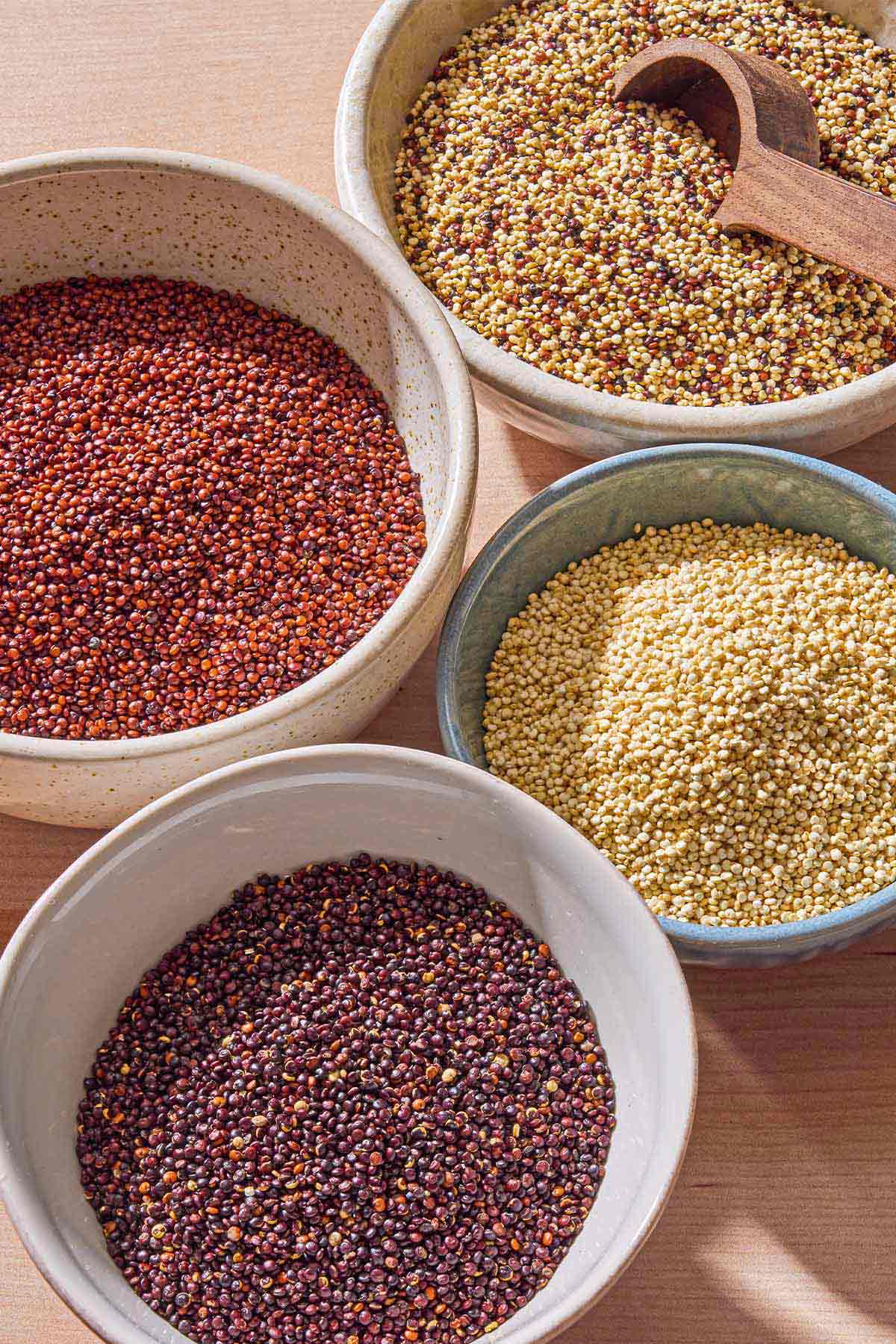 Bowls of red quinoa, white quinoa, black quinoa and rainbow quinoa with a spoon.