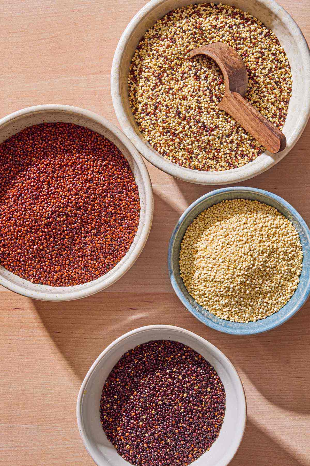 Bowls of red quinoa, white quinoa, black quinoa and rainbow quinoa with a spoon.