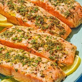 Four cooked lemon pepper salmon fillets on a platter with lemon wheels.