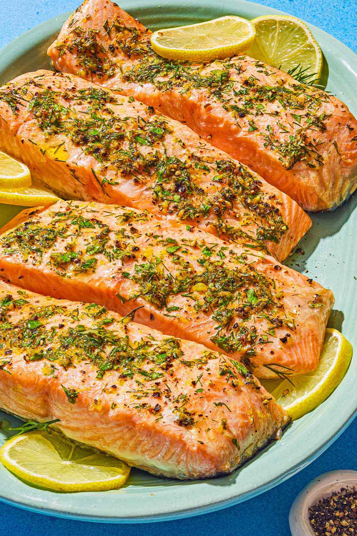 Four cooked lemon pepper salmon fillets on a platter with lemon wheels.