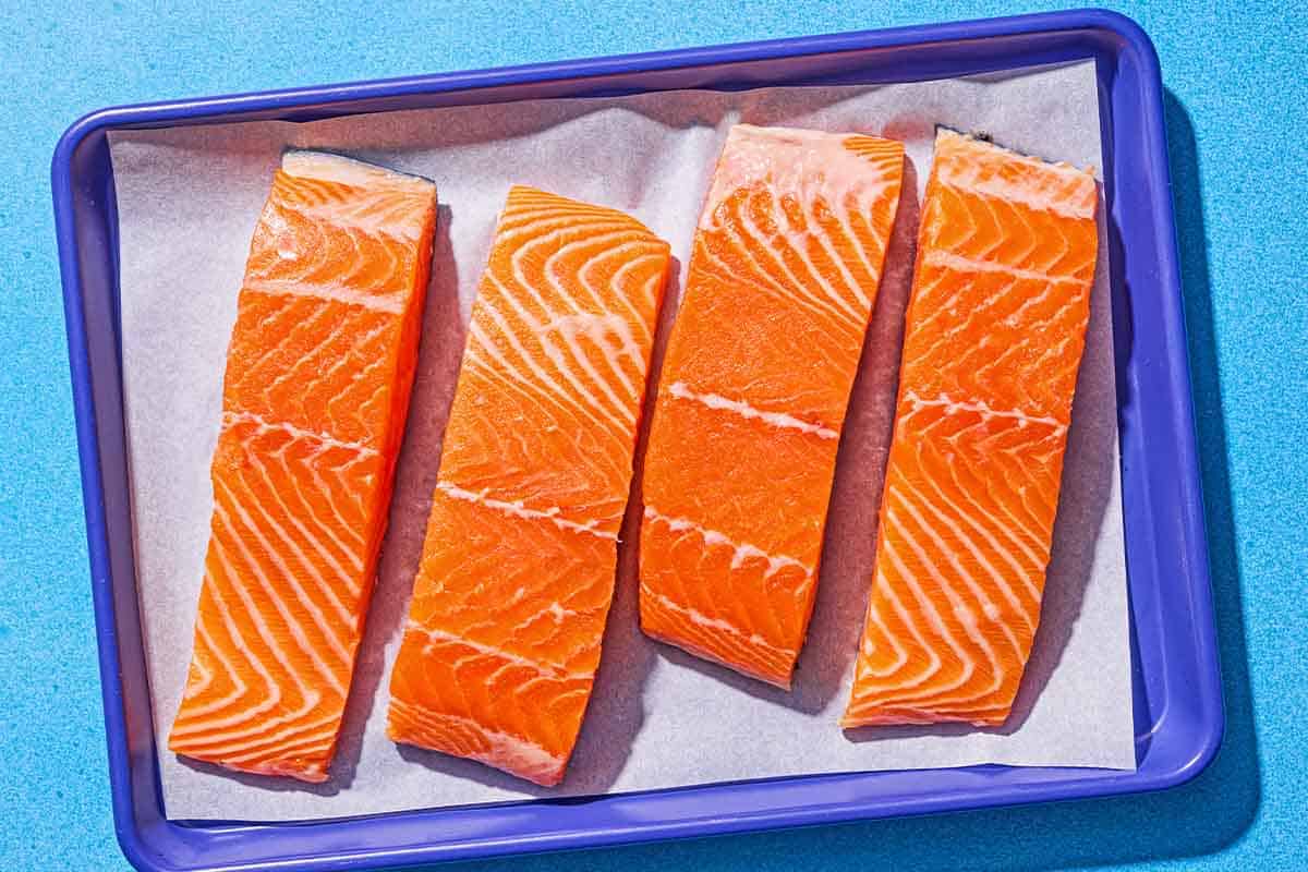Four uncooked salmon fillets on a parchment lined sheet pan.