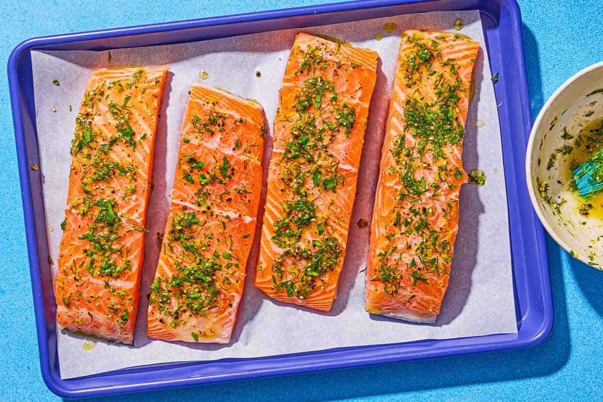 Four uncooked salmon fillets topped with the lemon pepper sauce on a parchment lined sheet pan. Next to this the bowl with the rest of the sauce.