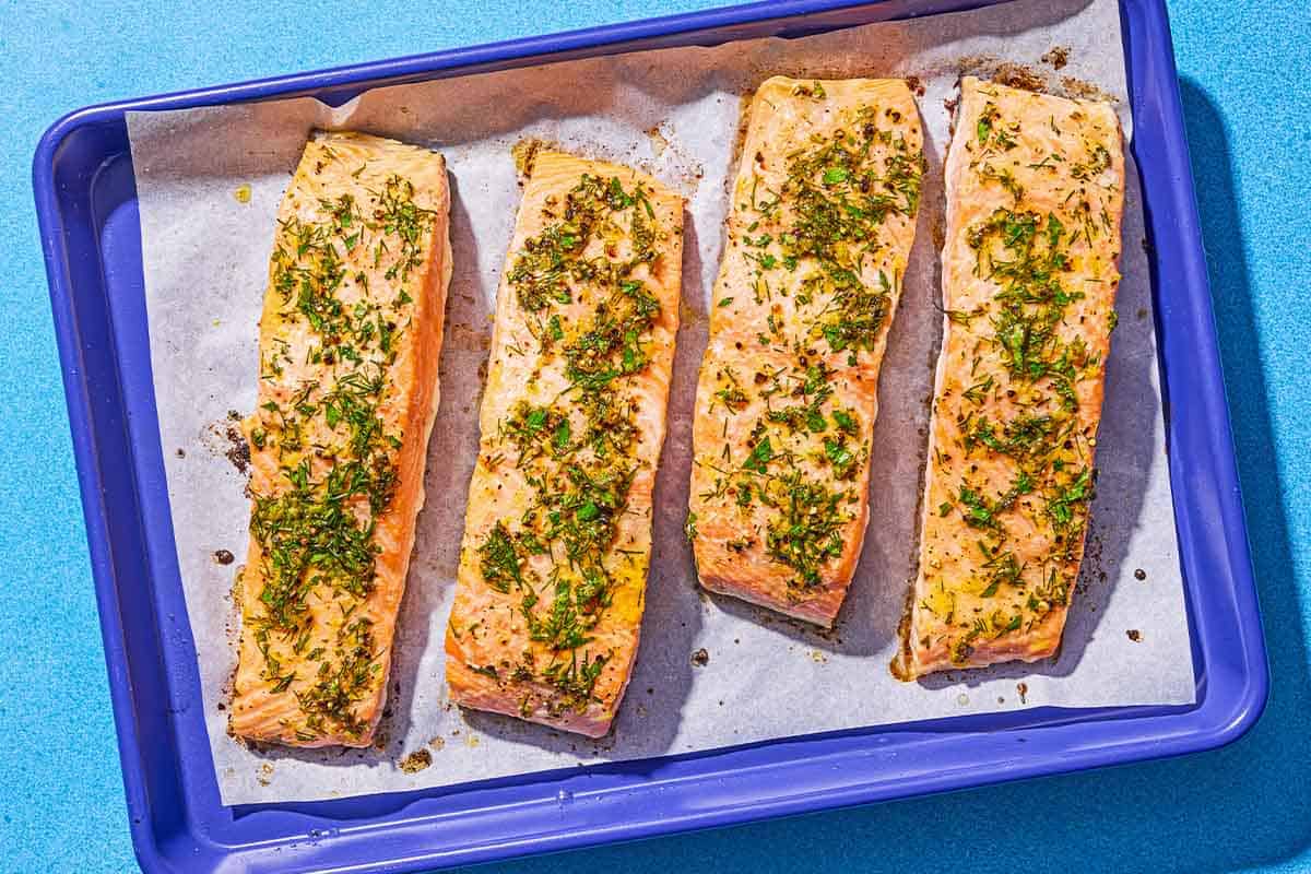 Four cooked lemon pepper salmon fillets on a parchment lined sheet pan.
