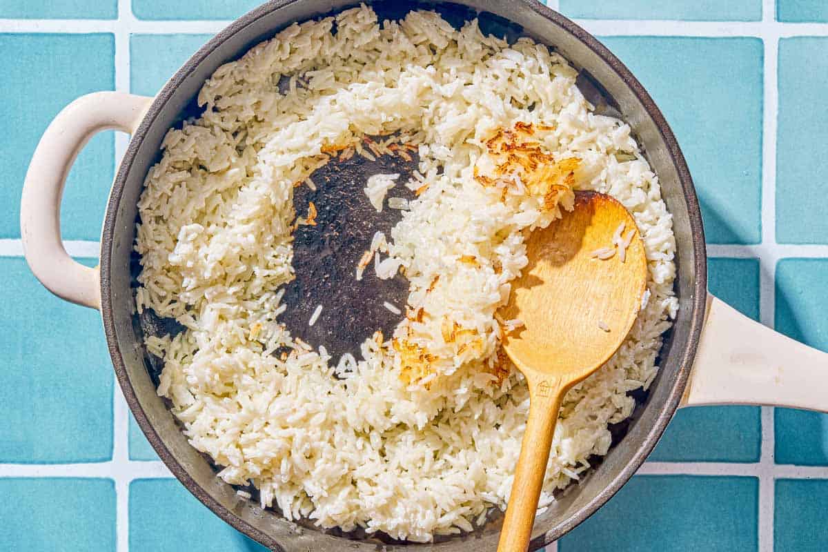 The rice for the salmon bowls being crisped in a skillet with a wooden spoon.