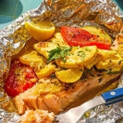 One serving of an open oven baked salmon in foil with vegetables on a plate with a fork.