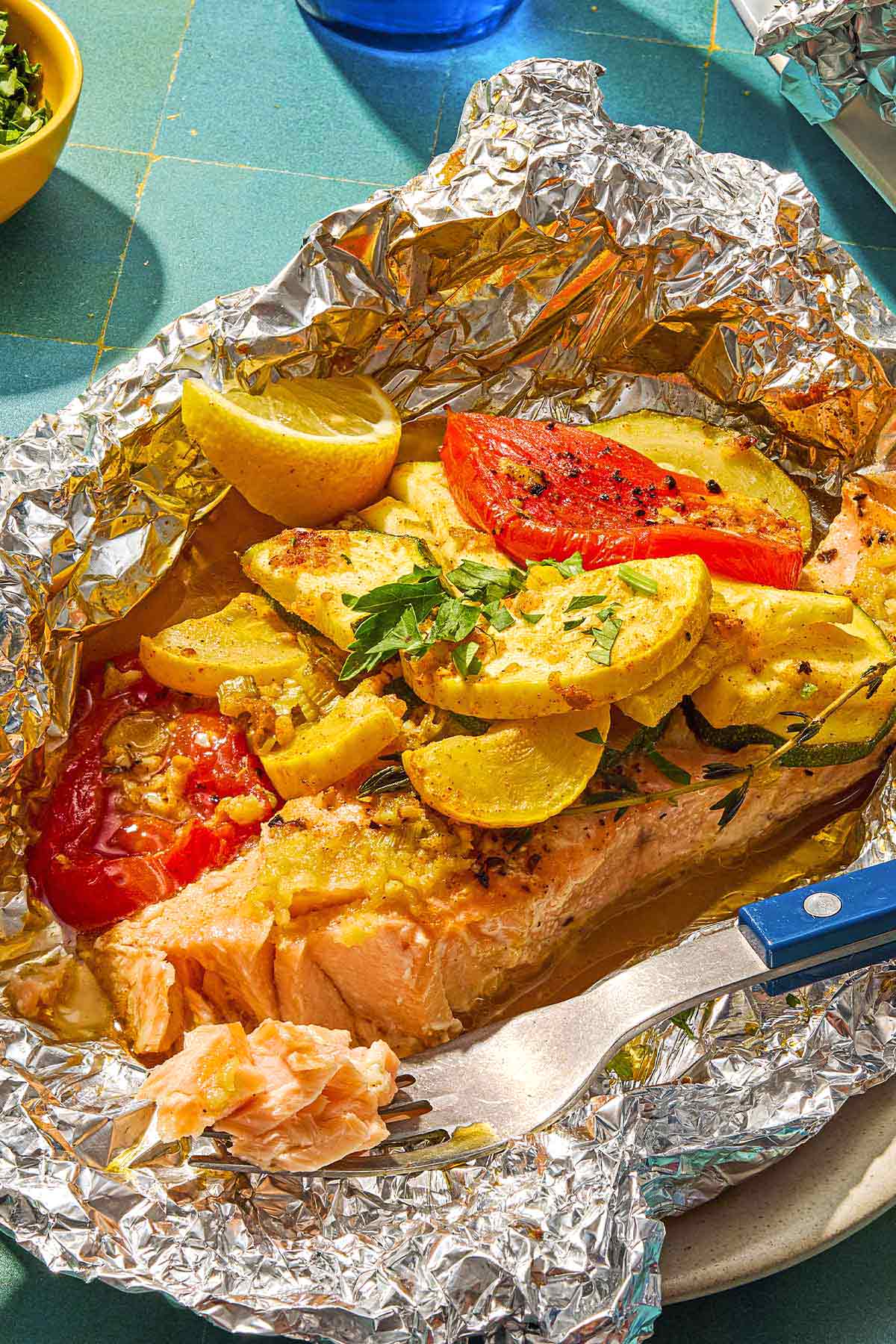 One serving of an open oven baked salmon in foil with vegetables on a plate with a fork.