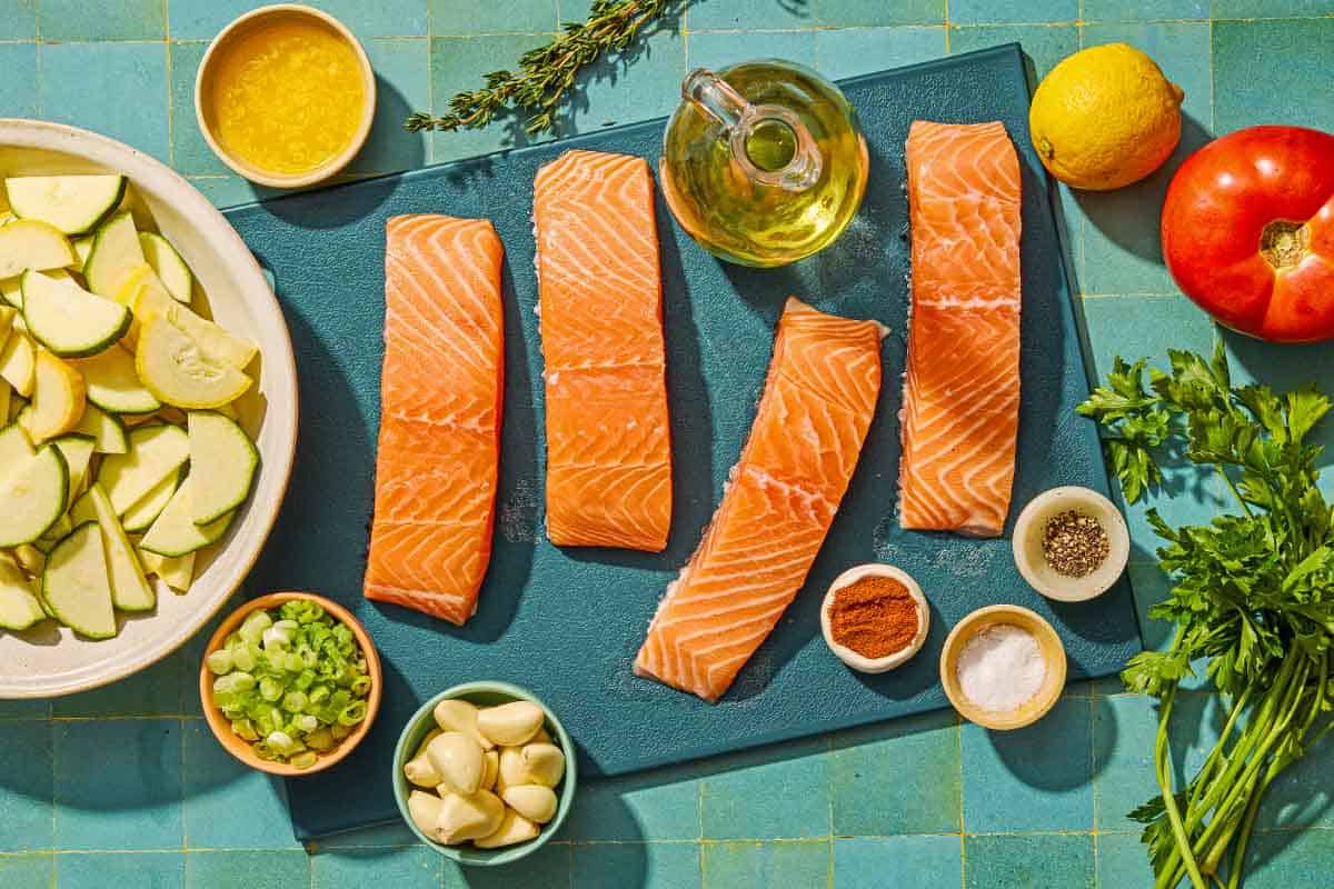 Ingredients for oven baked salmon in foil included 4 salmon fillets, olive oil, salt, pepper, garlic, thyme, summer squash, tomato, green onions, butter, paprika, lemon and parsley.