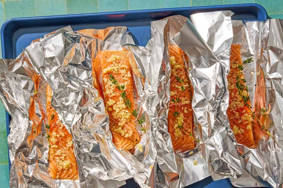 Four seasoned salmon fillets, each on a piece of foil on a sheet pan.