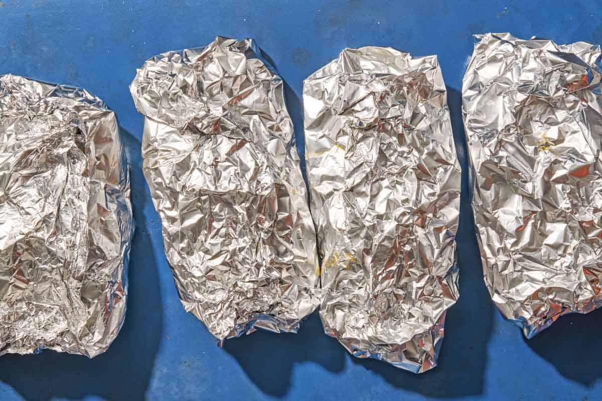 Four sealed servings of the oven baked salmon in foil with vegetables on a sheet pan.