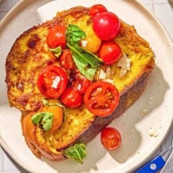 A slice of the savory french toast with the veggie topping on a plate next to a knife and fork.