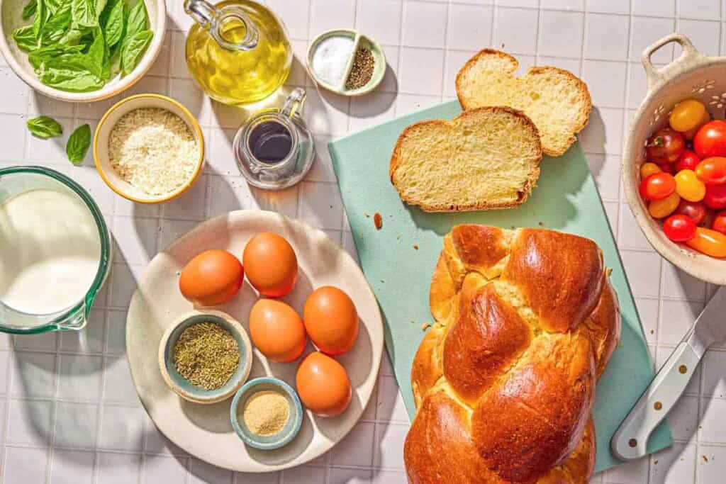 Ingredients for savory french toast including bread, eggs, milk, italian seasoning, garlic powder, salt, pepper, olive oil, parmigiano reggiano cheese, cherry tomatoes, balsamic vinegar, and fresh basil.