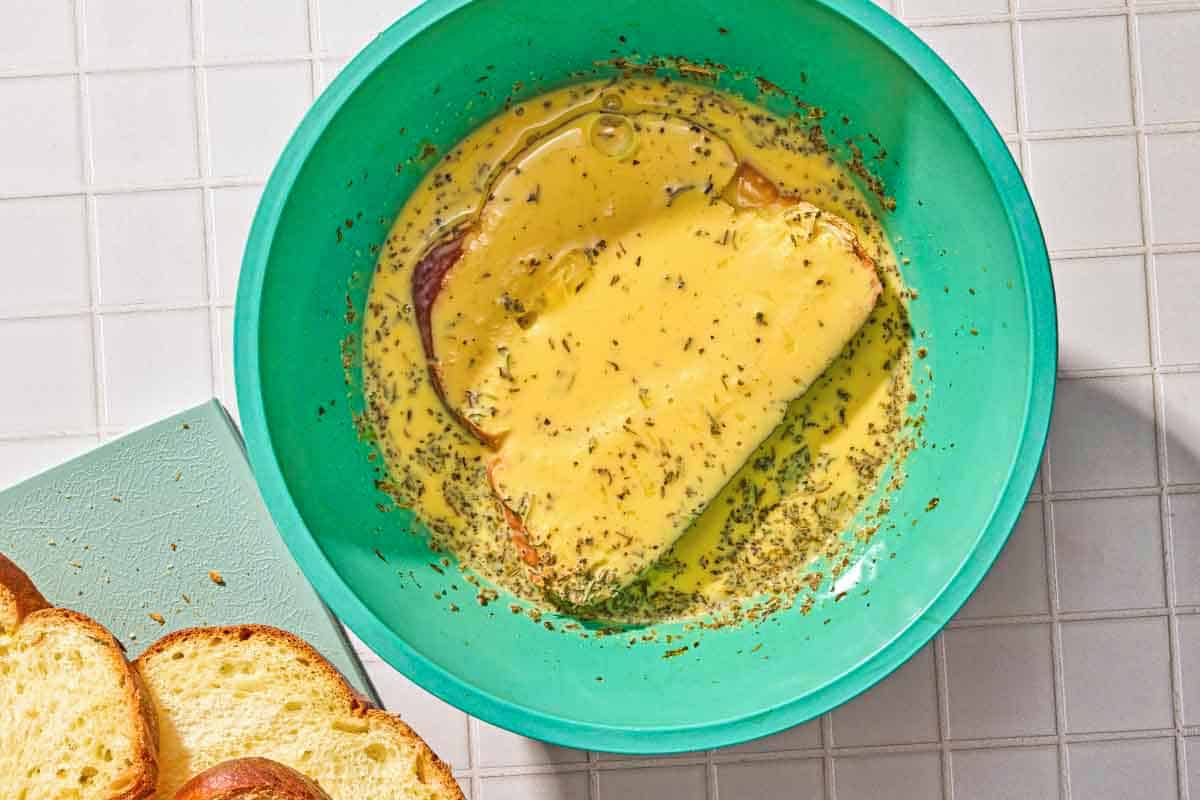 A slice of bread for the savory french toast in the custard in a bowl.