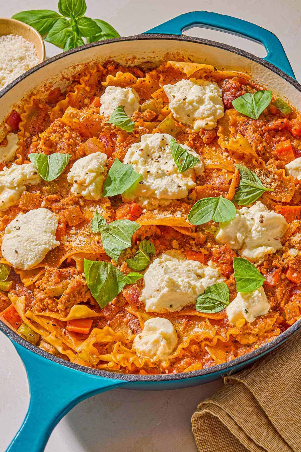 Skillet lasagna in a skillet next to basil leaves and a small bowl of Parmesan cheese.