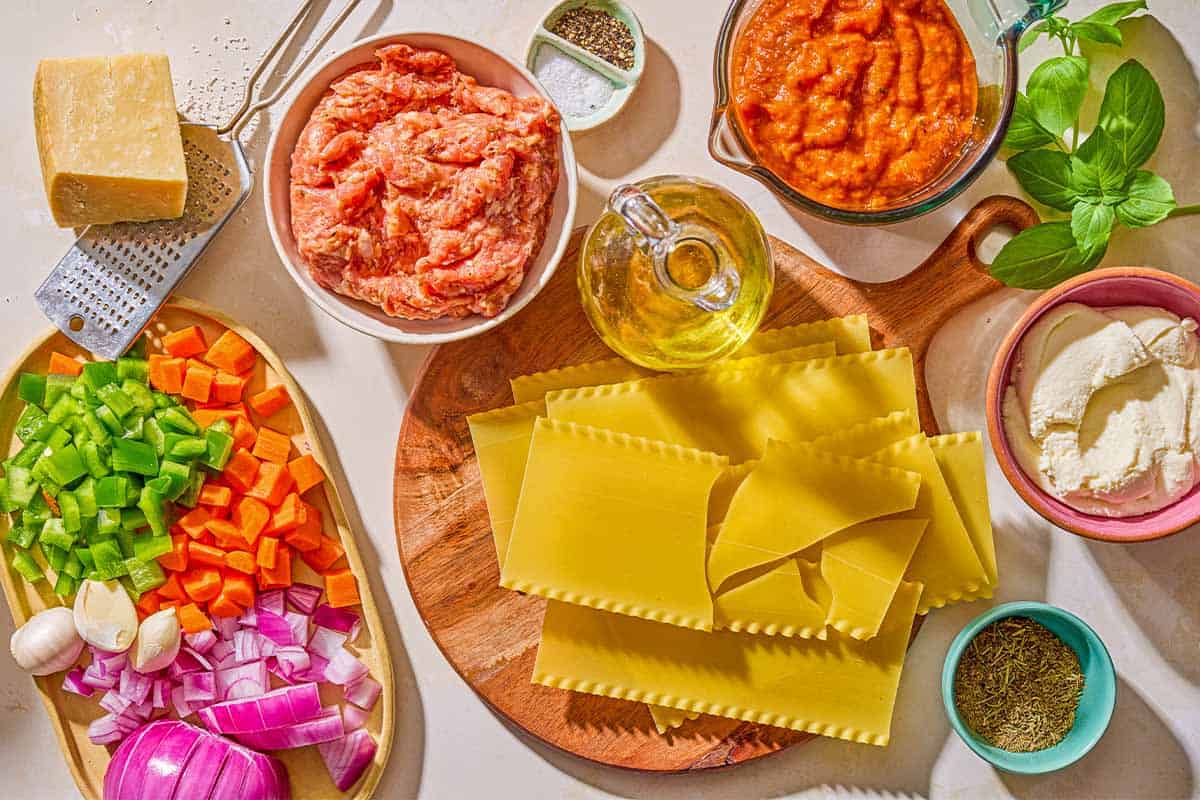 Ingredients for skillet lasagna including mild Italian pork sausage, olive oil, red onion, carrot, green bell pepper, garlic, marinara sauce, lasagna noodles, ricotta, Parmesan cheese, salt, pepper and fresh basil.