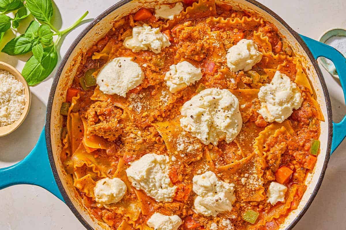 The skillet lasagna in a skillet next to a bowl of Parmesan and a sprig of fresh basil.