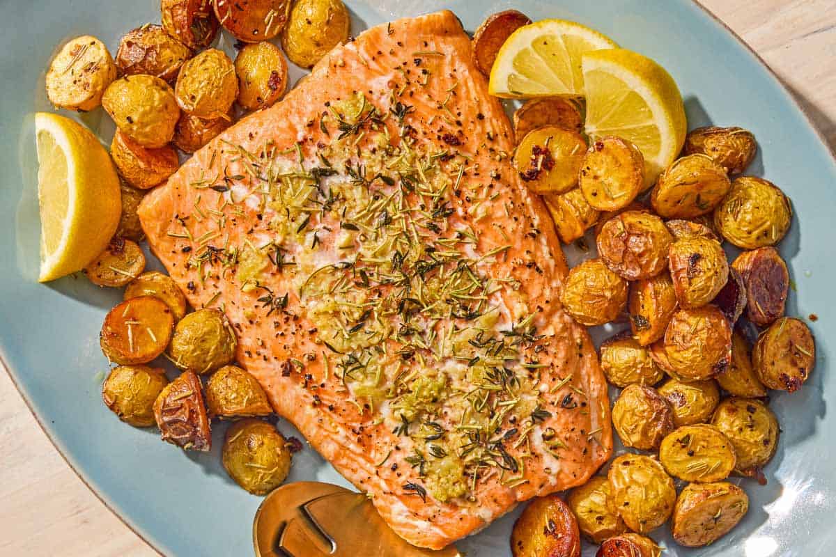 The slow roasted salmon and potatoes on a platter with lemon wedges and serving utensils.