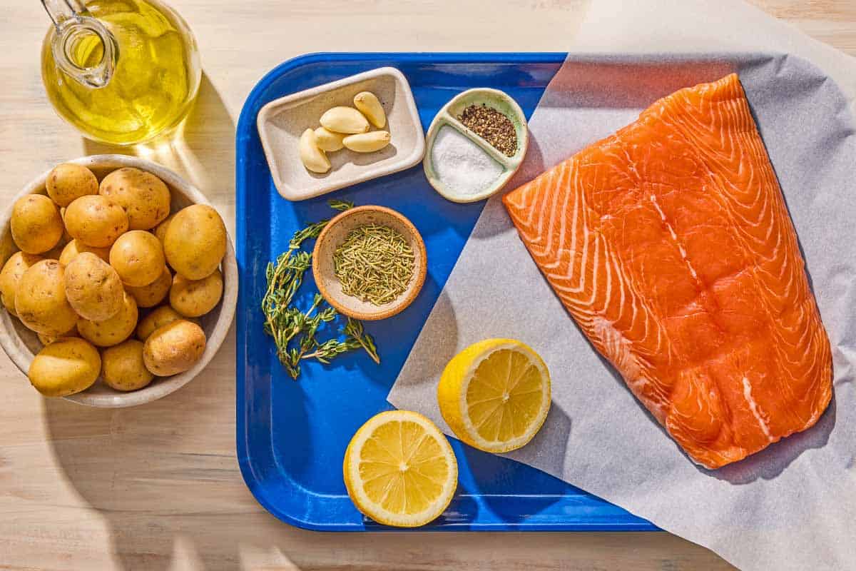 Ingredients for slow roasted salmon including salmon, lemon, salt, pepper, garlic, potatoes, olive oil, rosemary and thyme.