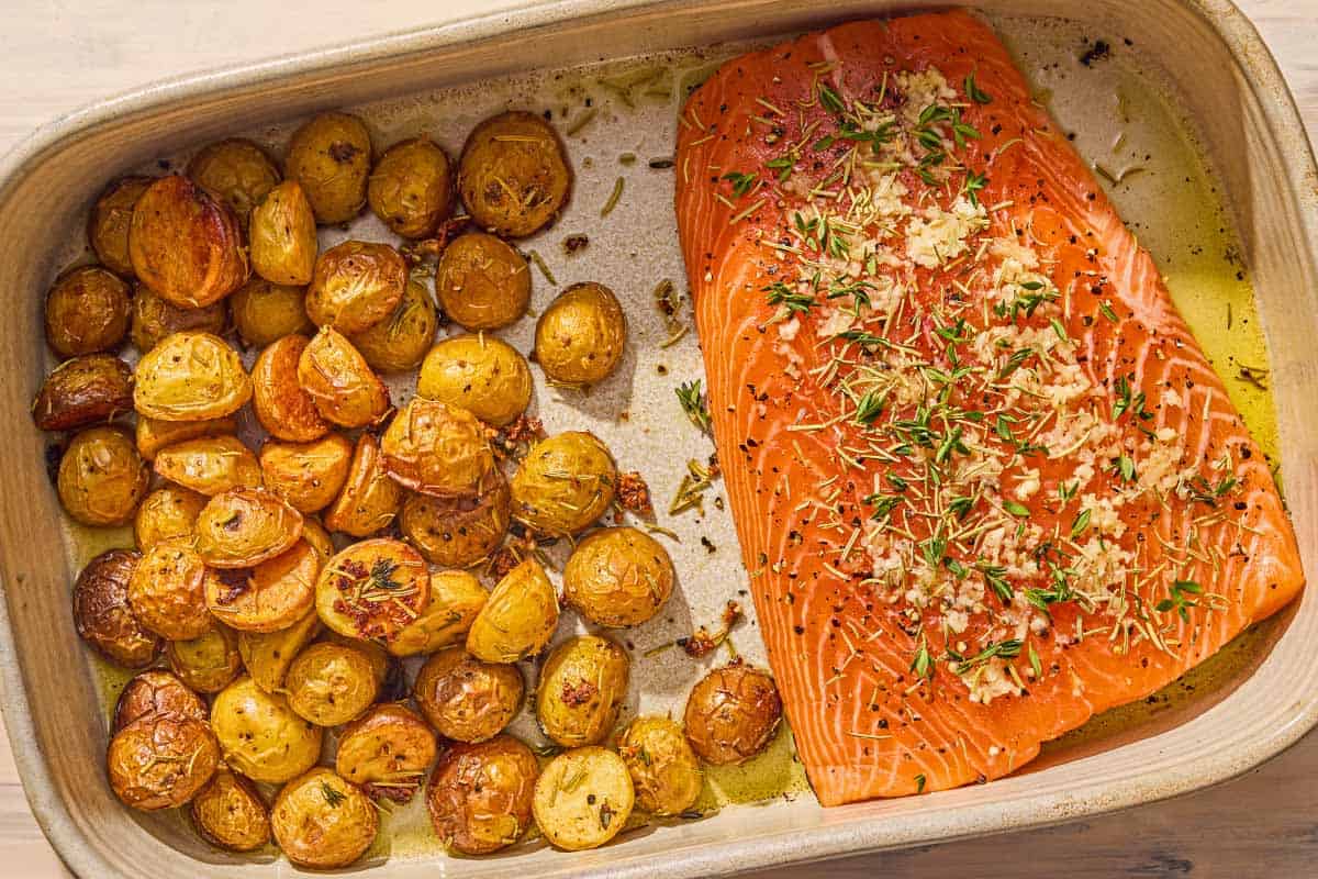 The roasted potatoes in a baking dish with the uncooked, seasoned salmon.