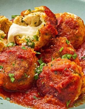 Mozzarella stuffed meatballs on a plate, with one split open showing the mozzarella cheese inside.