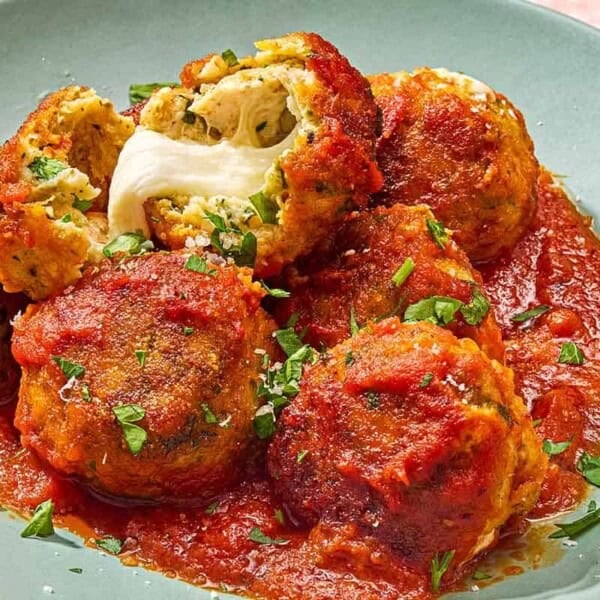 Mozzarella stuffed meatballs on a plate, with one split open showing the mozzarella cheese inside.