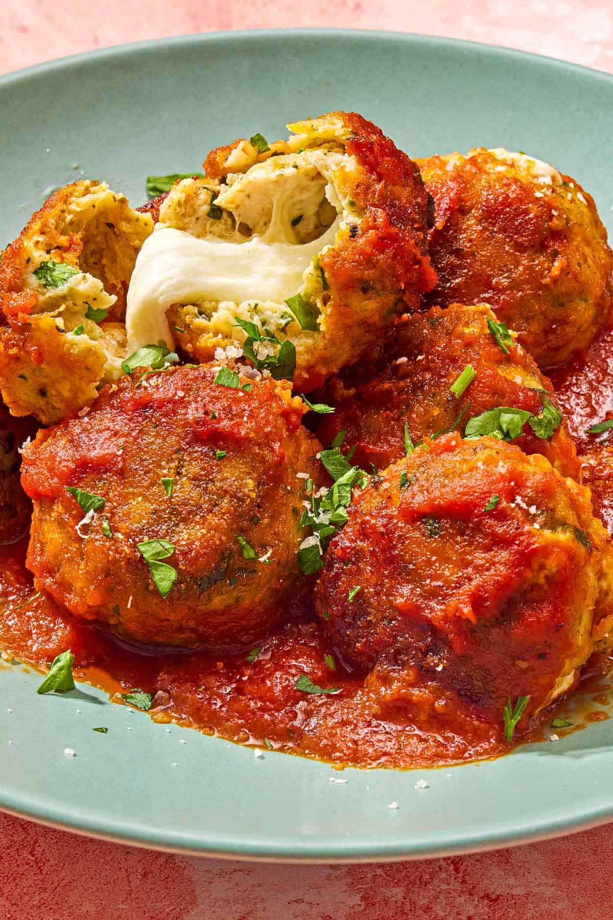 Mozzarella stuffed meatballs on a plate, with one split open showing the mozzarella cheese inside.