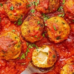 A close up of mozzarella stuffed meatballs in a skillet with a serving spoon holding a meatball that is split open, showing the mozzarella cheese inside.