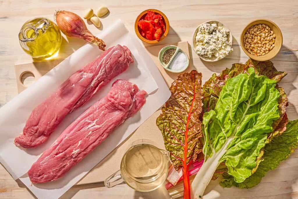 Ingredients for stuffed pork tenderloin including 2 pork tenderloins, pine nuts, olive oil, shallot, garlic, salt, pepper, sun dried tomatoes, goat cheese, and white wine.