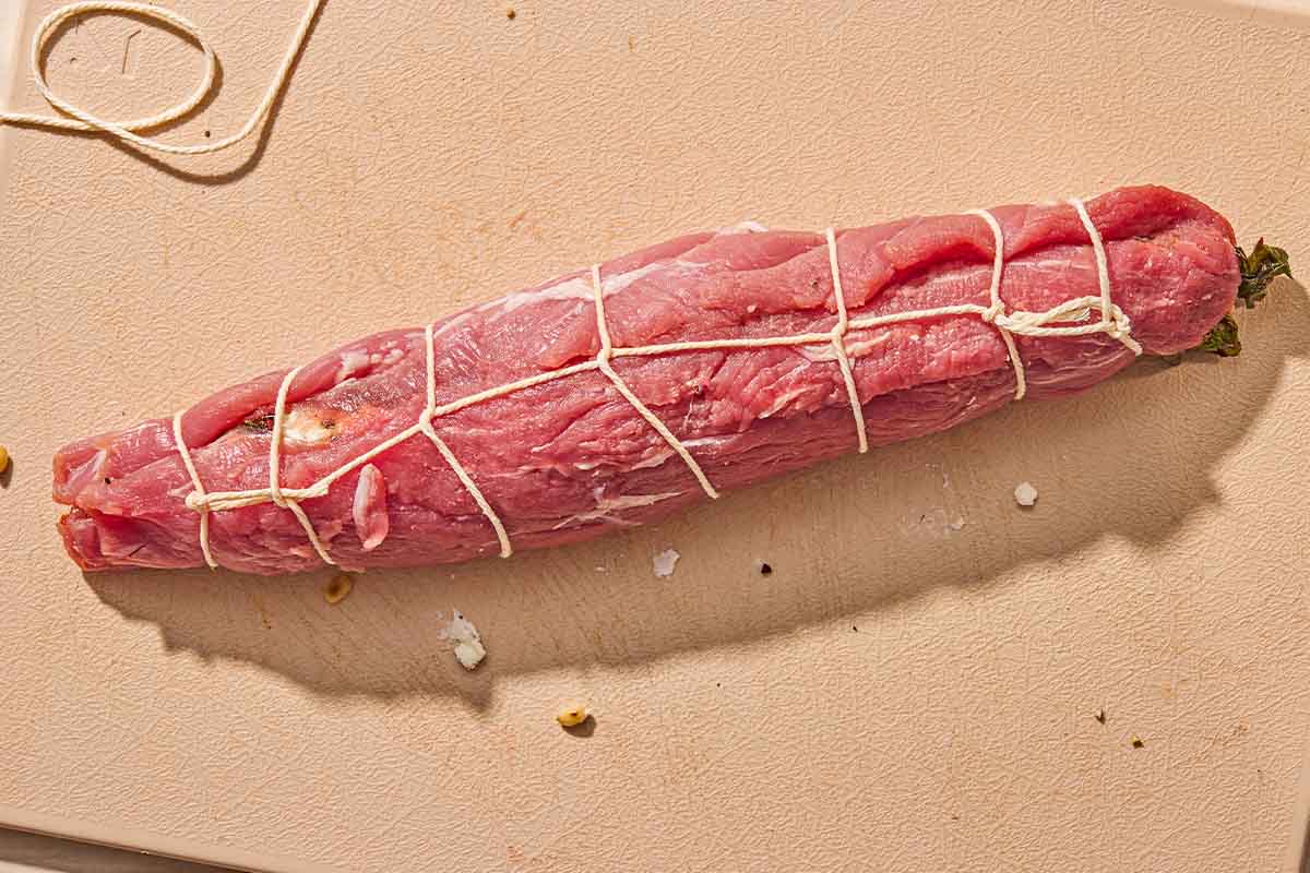 The uncooked stuffed pork tenderloin tied with twin on a cutting board.