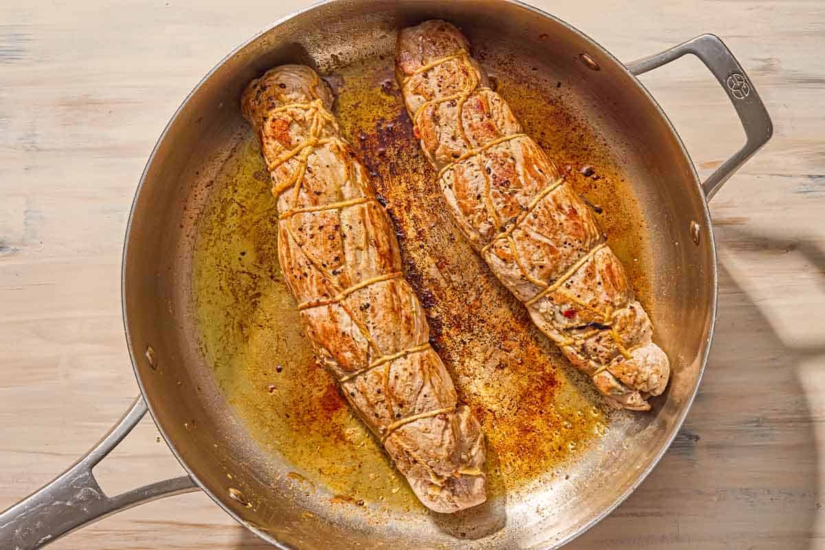 Two whole pork tenderloins being being seared in a skillet.