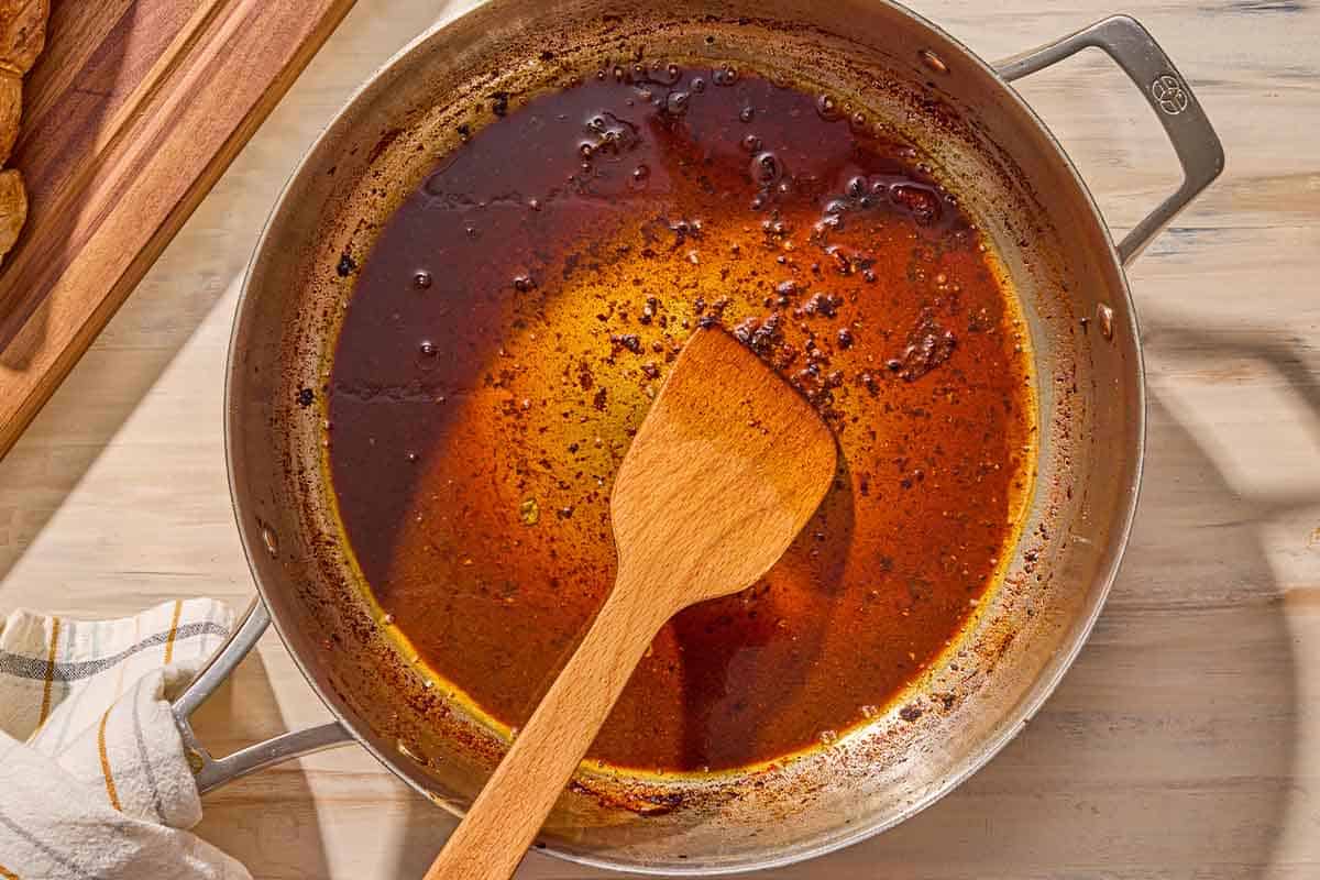 The wine and pan juices simmering together in a skillet with a wooden spatula.