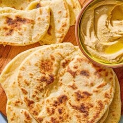 The pieces of the flatbread recipe on a wooden serving board with a bowl of hummus.