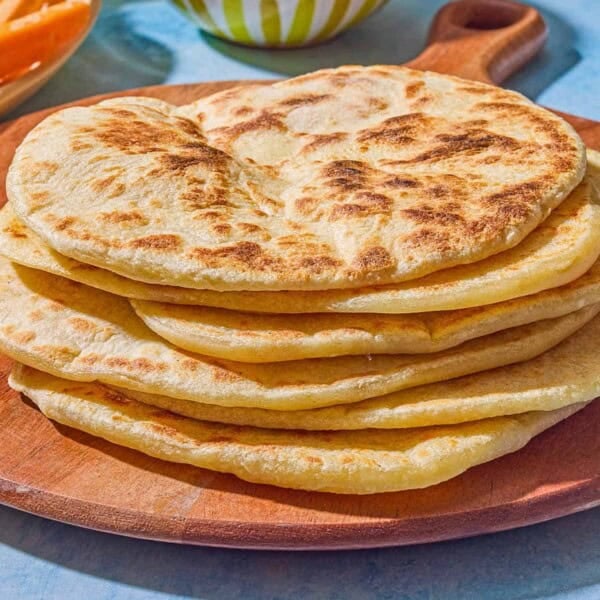 6 pieces of the flatbread recipe on a wooden serving board. Next to this is a bowl of hummus.