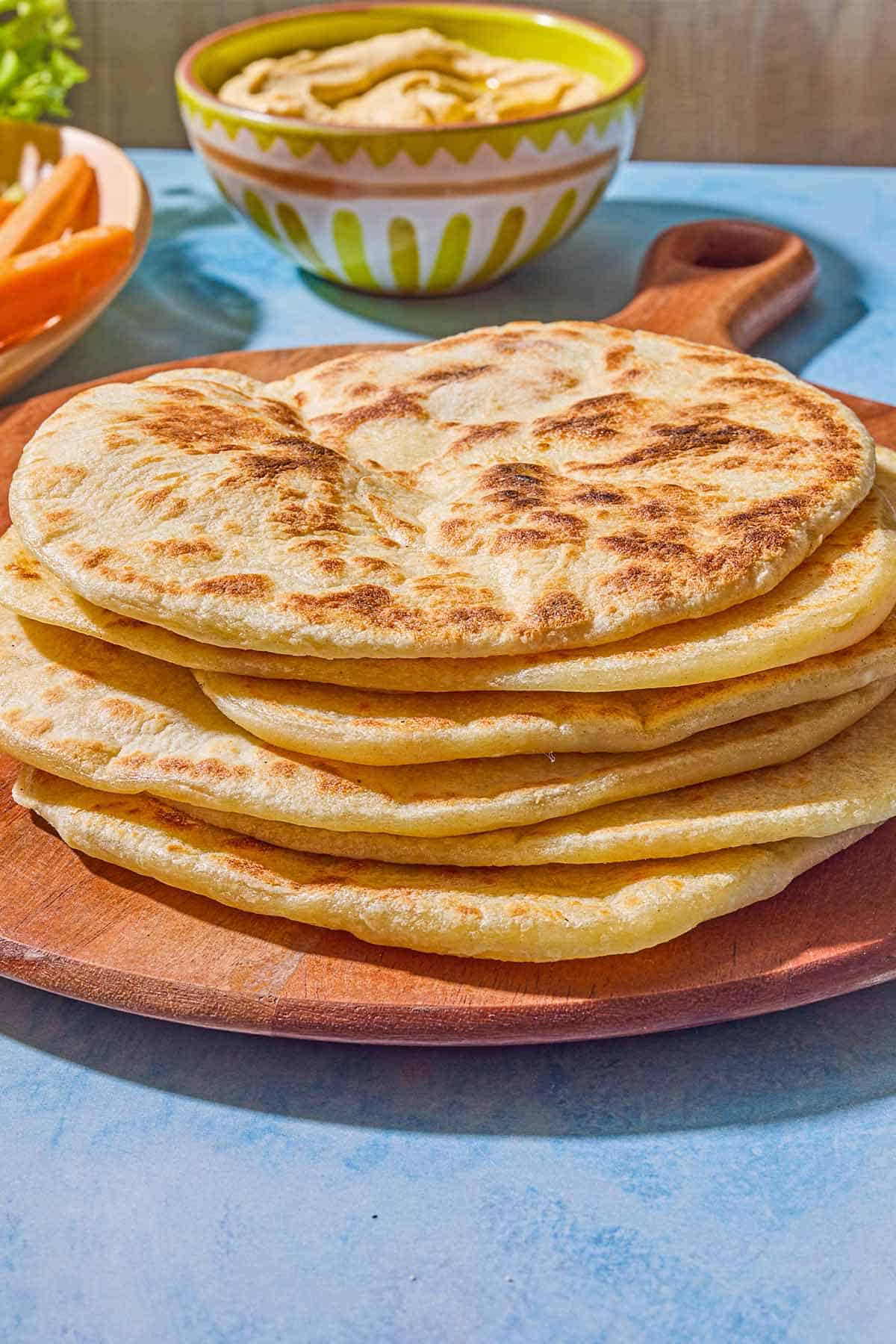 6 pieces of the flatbread recipe on a wooden serving board. Next to this is a bowl of hummus.