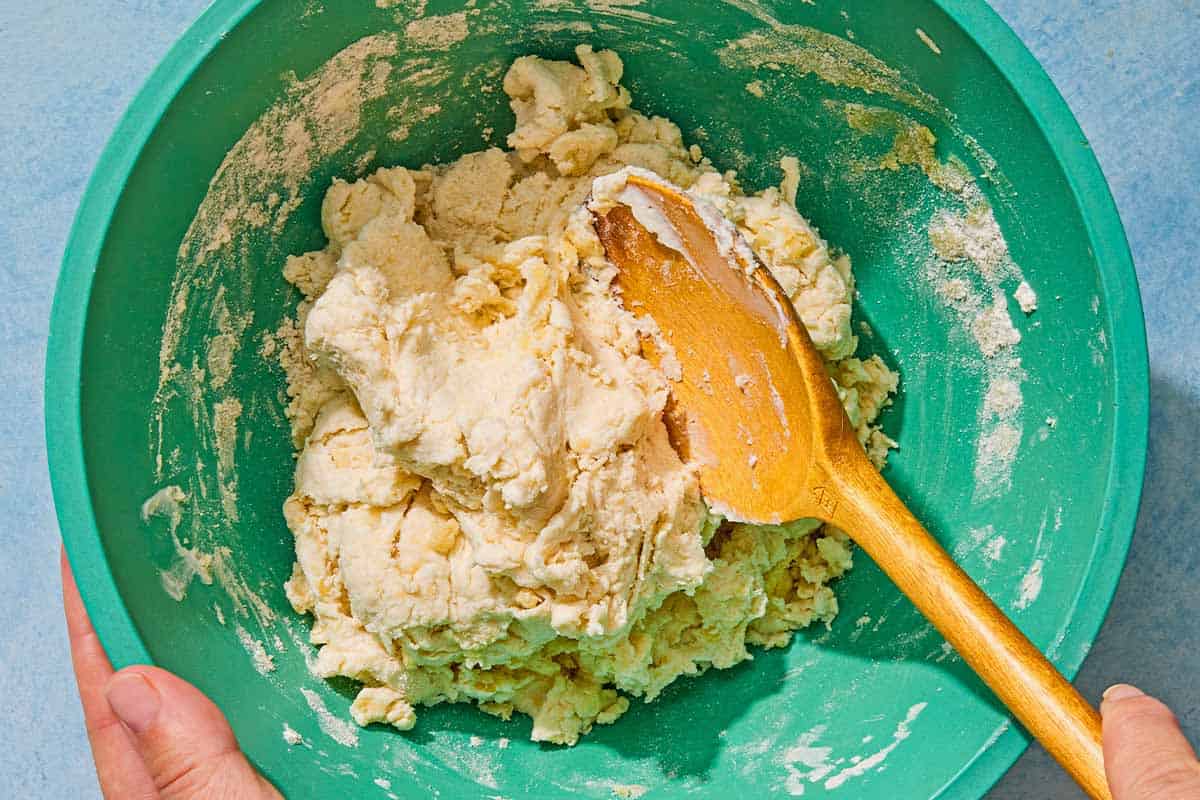 The dough for the flatbread recipe being mixed together in a bowl with a wooden spoon.