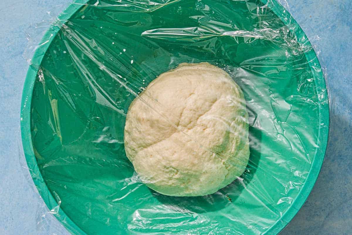 The dough for the flatbread recipe rising in a bowl covered with plastic wrap.