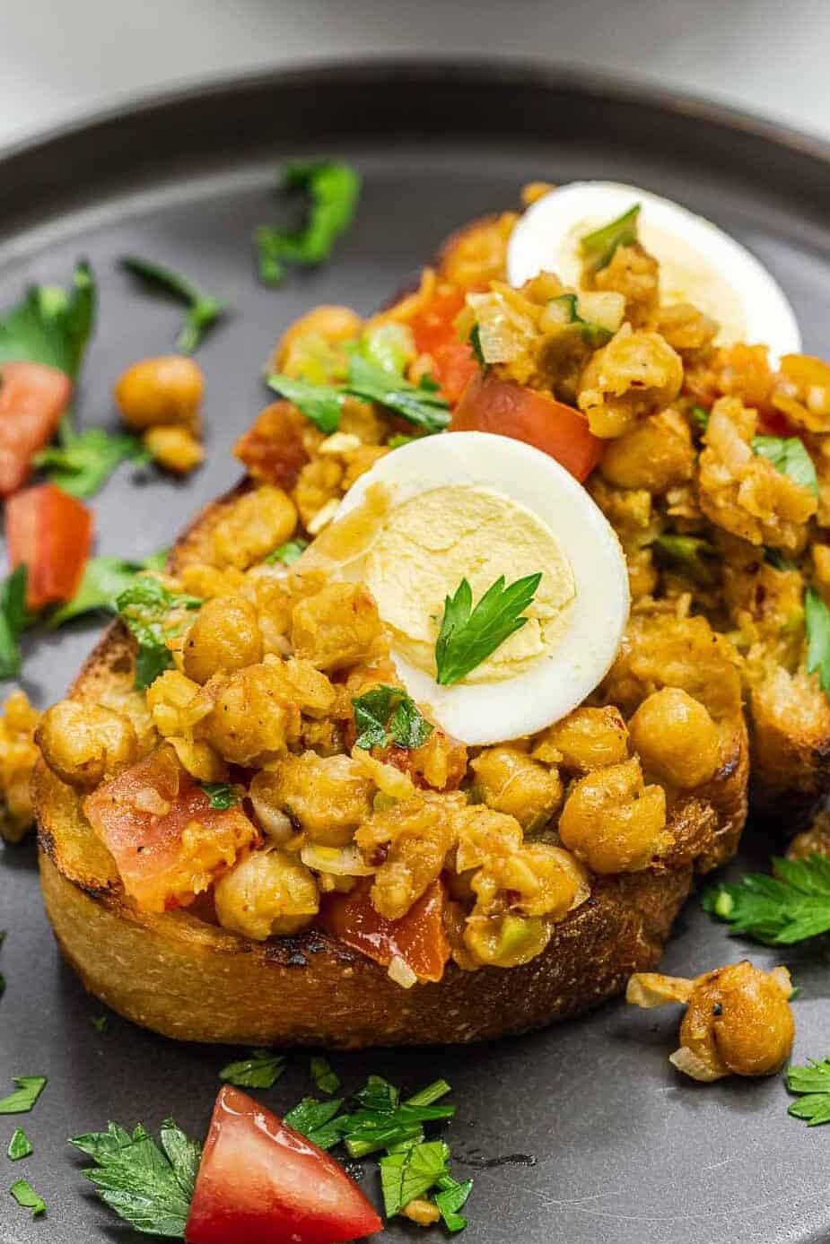 chickpeas on toast with eggs on top on a dark plate.
