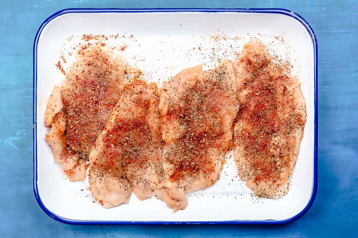 Uncooked seasoned chicken breasts on a small sheet pan.